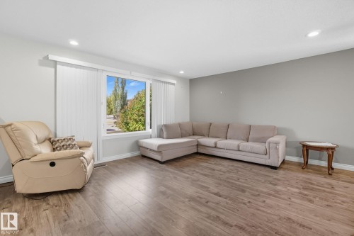 Spacious living area featuring wood-finish flooring, a large window with vertical blinds, recessed lighting, and light gray painted walls - 14239 53 Street, Edmonton, AB 
