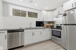 Modern kitchen featuring white cabinetry with matte black hardware, stainless steel appliances, a gray countertop, and a white subway tile backsplash - 