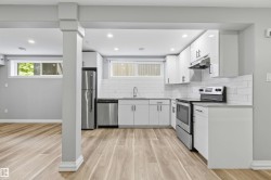 Open-concept kitchen featuring wood-finish flooring, white cabinetry, stainless steel appliances, a subway tile backsplash, and recessed lighting - 