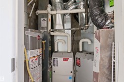 Utility closet featuring a water heater, two furnace units, and extensive ductwork - 