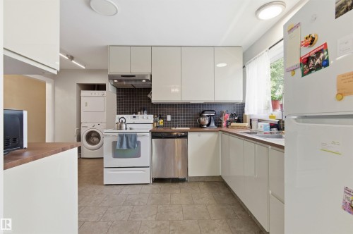 Kitchen featuring white flat-panel cabinetry, wood-finish countertops, tile flooring, and a dark tile backsplash - 7412/7414 83 Avenue, Edmonton, AB 