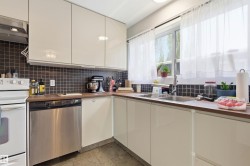 Kitchen featuring flat-panel cabinetry, a stainless steel dishwasher, wood-finish countertops, and a tile backsplash - 