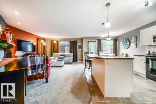 Open-concept living space featuring a kitchen island with seating, pendant lighting, stainless-steel sink, and a glass-paneled door leading to an exterior area - 8507 2 Avenue, Edmonton, AB - Indoor Photo Showing Kitchen