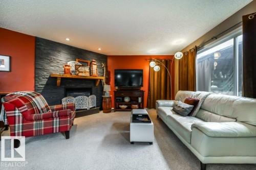 Living area featuring a textured stone-finish fireplace surround with a wood mantel, soft carpeting, recessed lighting, and a sliding glass door - 8507 2 Avenue, Edmonton, AB - Indoor Photo Showing Living Room With Fireplace