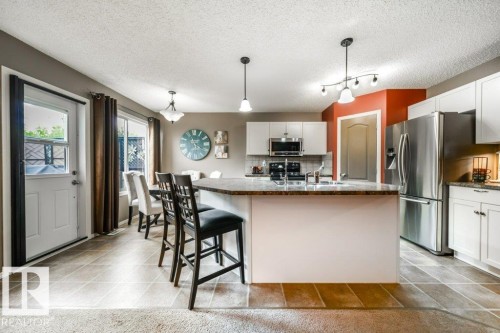 Open-concept kitchen featuring white cabinetry, stainless steel appliances, a multi-level island with seating, and a dining area - 8507 2 Avenue, Edmonton, AB - Indoor Photo Showing Kitchen With Upgraded Kitchen
