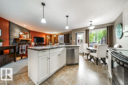Central kitchen island with white cabinetry and dark countertop, stainless steel dishwasher, tile flooring, glass sliding door, and a stone accent wall - 8507 2 Avenue, Edmonton, AB - Indoor Photo Showing Kitchen