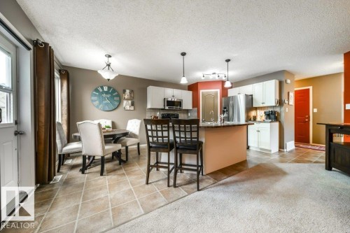Open-concept living space featuring a kitchen with white cabinetry and stainless steel appliances, a dining area with a chandelier, and a breakfast bar with pendant lighting - 8507 2 Avenue, Edmonton, AB - Indoor