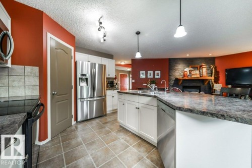 Kitchen featuring a large island with an integrated sink, white cabinetry, stainless steel appliances, and tile flooring - 8507 2 Avenue, Edmonton, AB - Indoor Photo Showing Kitchen With Double Sink With Upgraded Kitchen
