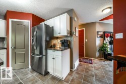 Kitchen area with white cabinetry, stainless steel refrigerator, and dark countertops - 
