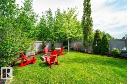 Expansive fenced backyard featuring a lush green lawn, mature trees, and a dedicated fire pit area - 