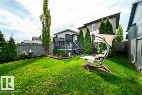 Expansive green lawn with a dark wood privacy fence, bordered by garden beds with dark mulch and mature evergreen plantings - 8507 2 Avenue, Edmonton, AB - Outdoor