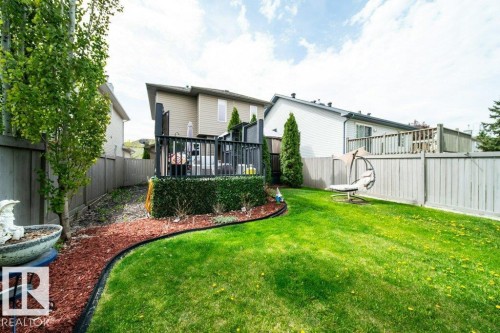 Landscaped backyard featuring a manicured lawn, a two-story deck with dark railings, a privacy fence, and mature trees - 8507 2 Avenue, Edmonton, AB - Outdoor With Deck Patio Veranda