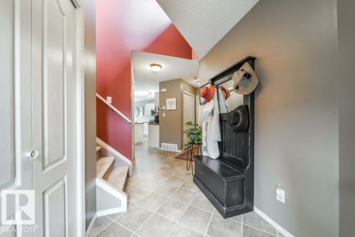 Entryway featuring durable square tile flooring, a built-in hall tree with storage bench, and a carpeted staircase with white risers - 8507 2 Avenue, Edmonton, AB - Indoor Photo Showing Other Room