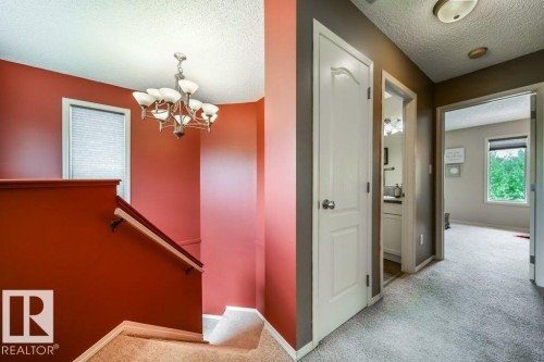 Staircase featuring a wood-finish handrail, neutral carpeting, and a decorative chandelier - 8507 2 Avenue, Edmonton, AB - Indoor Photo Showing Other Room