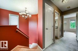 Staircase featuring a wood-finish handrail, neutral carpeting, and a decorative chandelier - 