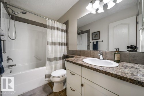 Bathroom featuring a white vanity with an undermount sink, a countertop with a stone-look finish, and a tile backsplash - 8507 2 Avenue, Edmonton, AB - Indoor Photo Showing Bathroom