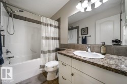 Bathroom featuring a white vanity with an undermount sink, a countertop with a stone-look finish, and a tile backsplash - 