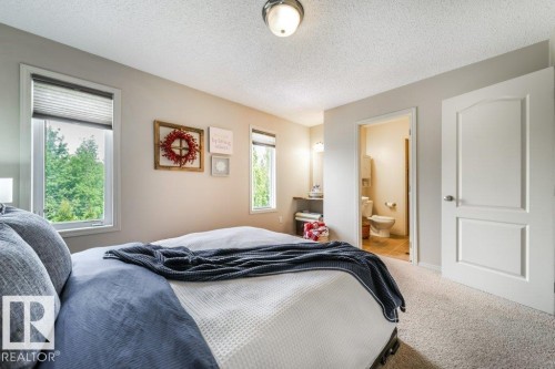 Carpeted bedroom featuring two large windows with blinds, a white two-panel door, and an attached bathroom with a vanity and toilet - 8507 2 Avenue, Edmonton, AB - Indoor Photo Showing Bedroom