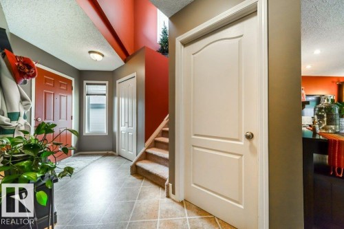 Entryway featuring durable tile flooring, a red paneled front door, a white bi-fold closet door, and a staircase with carpeted treads - 8507 2 Avenue, Edmonton, AB - Indoor Photo Showing Other Room