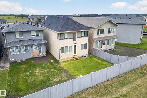 Rear exterior featuring a neutral tone facade, dark shingle roof, multiple windows, and a partially grassed backyard - 19286 22A Avenue, Edmonton, AB 