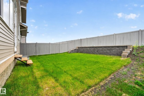 Expansive backyard featuring a lush lawn, privacy fencing, and a tiered retaining wall with integrated steps - 19286 22A Avenue, Edmonton, AB 