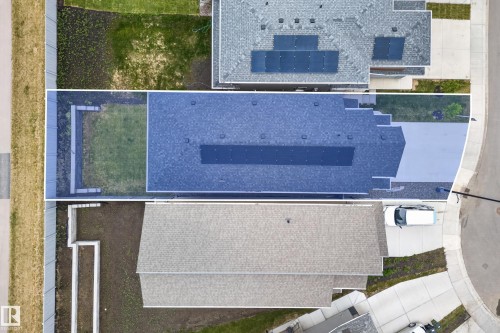 Overhead property view featuring a dark shingle roof, asphalt driveway, and a partially fenced rear yard with a grass area and concrete retaining walls - 19286 22A Avenue, Edmonton, AB 