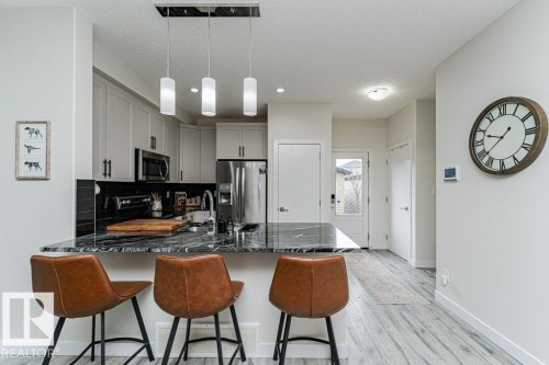 Kitchen featuring light gray cabinetry, stainless steel appliances, a dark stone countertop island with pendant lighting, and a black subway tile backsplash - 721 Berg Loop, Leduc, AB - Indoor Photo Showing Kitchen