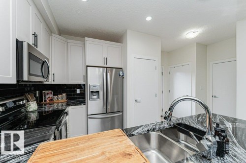 Contemporary kitchen featuring white cabinetry with black hardware, stainless steel appliances, black subway tile backsplash, and a double basin stainless steel sink with a high-arc faucet - 721 Berg Loop, Leduc, AB - Indoor Photo Showing Kitchen With Stainless Steel Kitchen With Upgraded Kitchen
