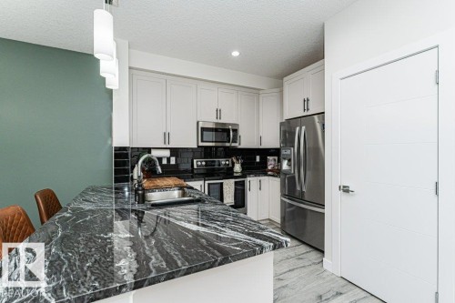 Modern kitchen featuring a large island with a dark, veined countertop, stainless steel appliances, white cabinetry with dark hardware, a black subway tile backsplash, and recessed ceiling lighting - 721 Berg Loop, Leduc, AB - Indoor Photo Showing Kitchen With Stainless Steel Kitchen With Double Sink