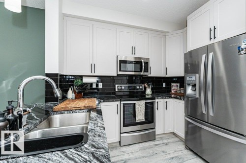 Modern kitchen featuring white shaker-style cabinetry, dark stone countertops with integrated stainless steel sink, a black subway tile backsplash, and stainless steel appliances - 721 Berg Loop, Leduc, AB - Indoor Photo Showing Kitchen With Stainless Steel Kitchen With Double Sink