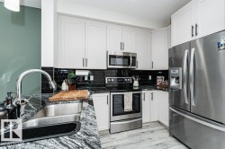 Modern kitchen featuring white shaker-style cabinetry, dark stone countertops with integrated stainless steel sink, a black subway tile backsplash, and stainless steel appliances - 