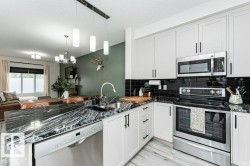 Modern kitchen featuring white shaker cabinetry with dark hardware, stainless steel appliances, black subway tile backsplash, and a patterned dark countertop - 