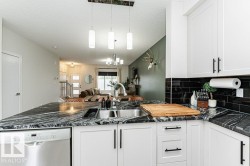 Kitchen island featuring a double basin stainless steel sink, black patterned countertop, white cabinetry with black hardware, and an integrated stainless steel dishwasher - 