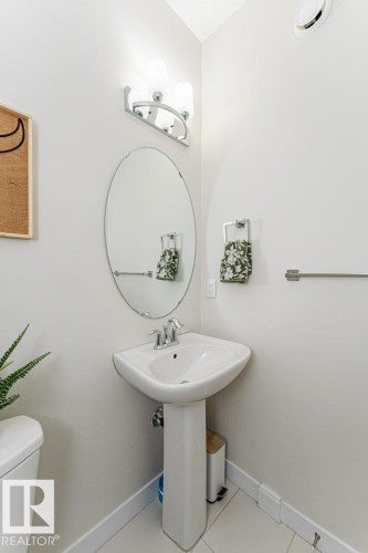 Pedestal sink with chrome faucet, an oval vanity mirror, and an overhead vanity light fixture - 721 Berg Loop, Leduc, AB - Indoor Photo Showing Bathroom