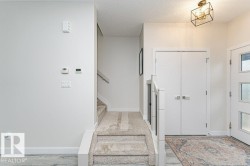 Entryway featuring a contemporary semi-flush mount light fixture, white interior doors with horizontal detailing, and carpeted stairs with a white and black railing - 