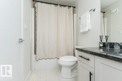 Modern bathroom featuring a vanity with dark stone countertop, white cabinetry with black hardware, and a tile shower with an opaque curtain - 