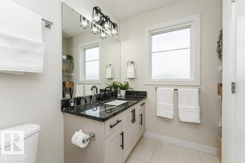 Bathroom featuring a dark stone countertop with integrated sink, white cabinetry with black hardware, a large vanity mirror, and a linear light fixture with four square shades - 721 Berg Loop, Leduc, AB - Indoor Photo Showing Bathroom