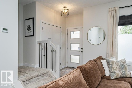 Entryway featuring a three-panel opaque glass door, a black metal cage ceiling light fixture, a staircase with white newel posts and black metal spindles, and light-colored carpeting - 721 Berg Loop, Leduc, AB - Indoor