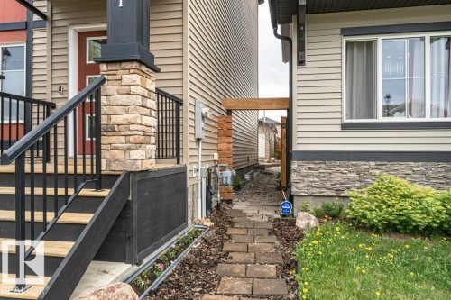 Exterior entryway featuring a stone veneer pillar, dark railing, and light wood-finish steps - 721 Berg Loop, Leduc, AB - Outdoor With Exterior