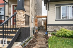 Exterior entryway featuring a stone veneer pillar, dark railing, and light wood-finish steps - 