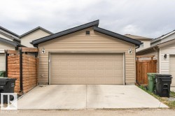 Rear detached garage with a paneled door, tan horizontal siding, black trim, and a black-shingled shed roof - 
