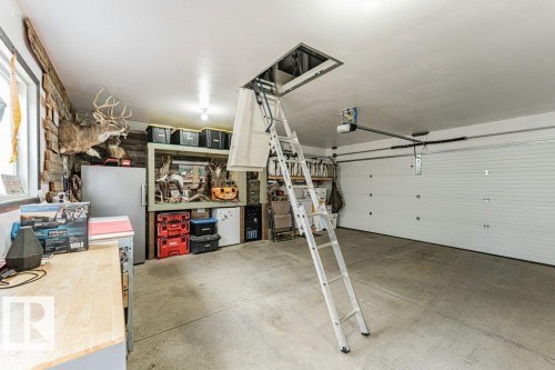 Spacious garage featuring concrete flooring, a white paneled garage door with an automatic opener, an attic access ladder, and a built-in workbench with storage - 721 Berg Loop, Leduc, AB - Indoor Photo Showing Garage
