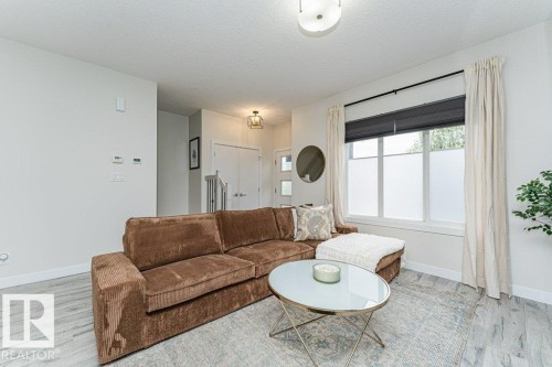Bright living area featuring wood-finish flooring, a large window with privacy film and roller shades, and a flush-mount ceiling light fixture - 721 Berg Loop, Leduc, AB - Indoor Photo Showing Living Room