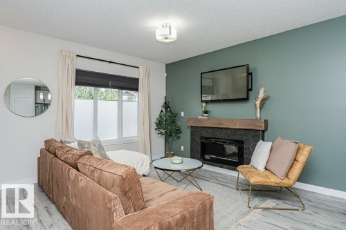 Living area featuring a modern fireplace with a wood-finish mantel and hexagonal tile surround - 721 Berg Loop, Leduc, AB - Indoor Photo Showing Living Room With Fireplace