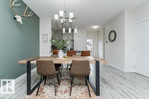 Dining area featuring a wood-finish table with black metal legs, an overhead multi-bulb chandelier, and light wood-finish flooring - 721 Berg Loop, Leduc, AB - Indoor Photo Showing Dining Room