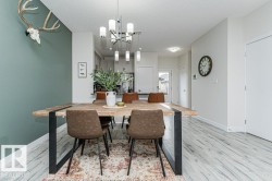Dining area featuring a wood-finish table with black metal legs, an overhead multi-bulb chandelier, and light wood-finish flooring - 