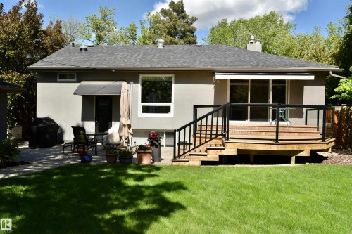 Expansive backyard featuring a manicured lawn, a multi-level wood deck with black railing and glass panels, and a concrete patio - 6 St George'S Crescent, Edmonton, AB 