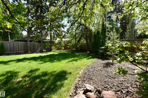 Expansive backyard featuring a manicured lawn, established perimeter fencing, mature trees, a landscaped bark-mulch bed, and natural rock accents - 6 St George'S Crescent, Edmonton, AB 