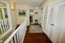 Hallway featuring wood-finish flooring, white louvered bifold doors, a white banister and railing, a wall sconce, and a doorway opening to another room - 6 St George'S Crescent, Edmonton, AB 