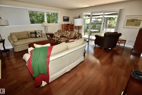 Spacious living area featuring polished wood-finish flooring, white walls, and a multi-pane glass sliding door providing access to the exterior patio - 6 St George'S Crescent, Edmonton, AB 